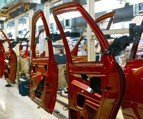 Proizvodna hala s nizom crvenih auto karoserija (vrata i okvir) na montažnoj, proizvodnoj liniji