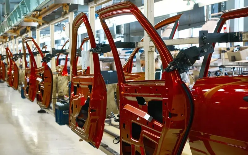 Proizvodna hala s nizom crvenih auto karoserija (vrata i okvir) na montažnoj, proizvodnoj liniji